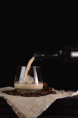 Cream liqueur is poured from a bottle into a glass. Dark background, vertical orientation. Coffee beans.