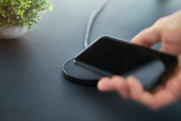 Need to recharge smartphone battery. Male hand laying down electronic device on wireless charger.