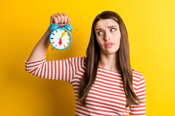 Portrait of attractive tired overwhelmed girl holding clock early hour morning isolated over bright yellow color background