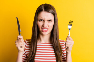 Portrait of attractive angry girl holding cutlery fast food meal snack isolated over bright yellow color background