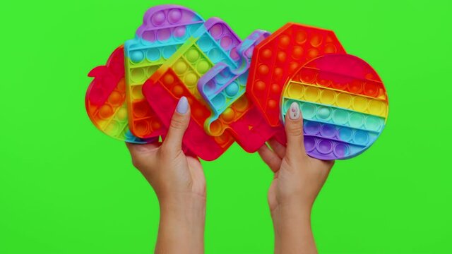 Hands showing many pop it sensory anti-stress toys isolated on chroma key. Girl with rainbow bubbles squishies games. Stress anxiety relief. Trendy fidgeting game for stressed children and adults
