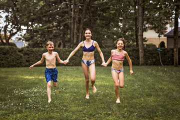 Fototapeta premium Happy beautiful childs running through rain in Swimsuits