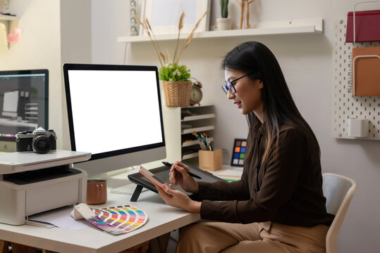 Asian woman designer working using a smartphone blank white computer screen placed at table with color samples. Mock up.