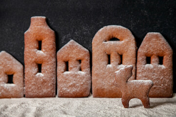 Homemade gingerbread town standing in row with Christmas deer sprinkled with powdered sugar on black background.