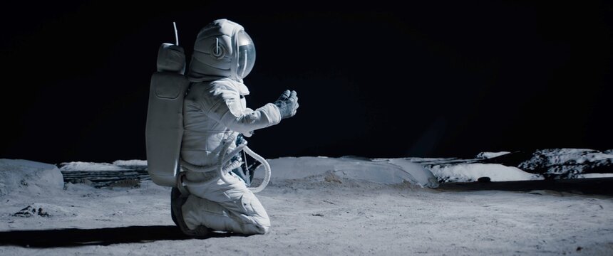 CU Portrait of Caucasian female lunar astronaut finds something and kneels while exploring Moon surface. Shot with 2x anamorphic lens