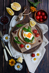 Vertical composition. Breakfast of a sandwich with egg, cheese and herbs, tomatoes on a dark wooden table. View from above.