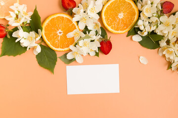 Citrus and strawberry slices with garden jasmine flowers with leaves and blank business card on orange background