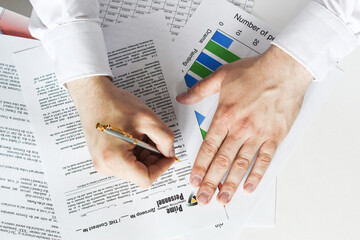 A businessman sitting at an office desk signs a contract with a shallow emphasis on signing....