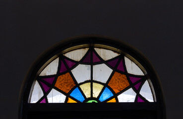 Semi-circular multicolored stained glass window and dark wall 