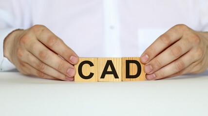 A businessman holds wooden cubes with a word CAD on a white background, with space to copy the text, business concept