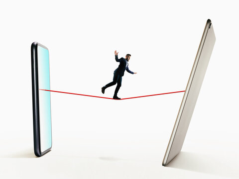 A man walks a tightrope from smartphone to digital tablet. Risk, balance concept.