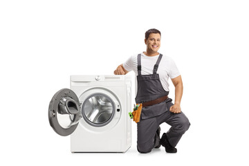 Repairman kneeling next to a washing machine and looking at camera