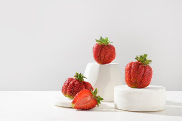 Fresh ugly strawberry on podium and stand on a white background. Concept homegrown organic eco products. Copy space.