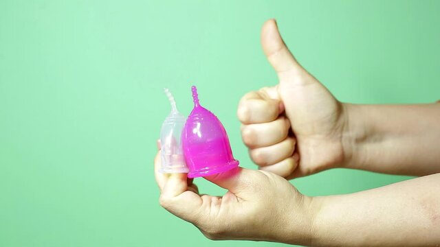 menstrual cups of different colors on a woman's palm on a green background