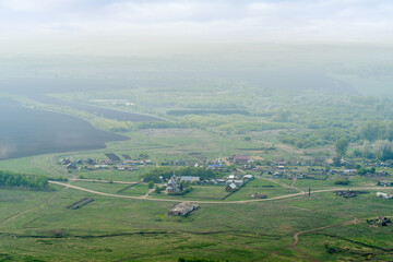 View from the mountain to the Russian village with a church and fields through a foggy haze. Photo taken near Andreevka village, Orenburg region, Russia