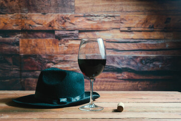 glass of red wine next to cork and fedora hat in cava