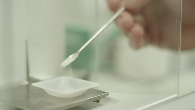 Researcher puts powder onto lab scale to measure weight of substance for tests