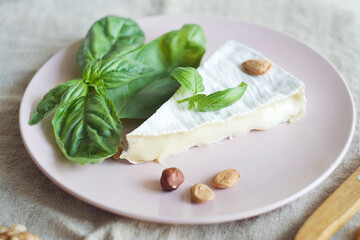 Soft cheese lies on a plate, next to it is basil leaves and nuts. Breakfast