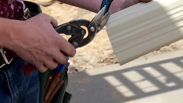 Snip or compound snips are used by worker hands to cut a section of aluminum rain gutter. Hand held closeup clip.