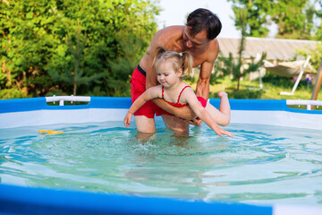 Obraz na płótnie Canvas Father teaching his toddler daughter how to swim. Child swimming lesson. Cute little girl with father in summer metal frame pool at home in the yard. Pool time. Home vacations. 
