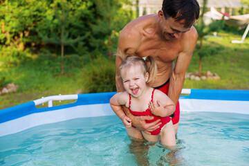Fototapeta na wymiar Father teaching his toddler daughter how to swim. Child swimming lesson. Cute little girl with father in summer metal frame pool at home in the yard. Pool time. Home vacations. 