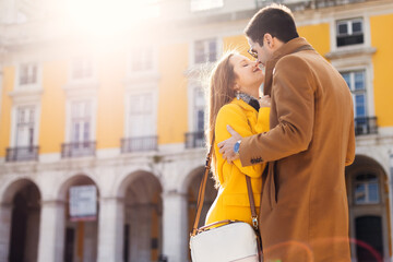 happy woman and man in sunglasses hugging and kissing on the street against the background of the building