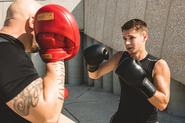 Two men exercising and fighting in outside. Boxer in gloves is training with a coach