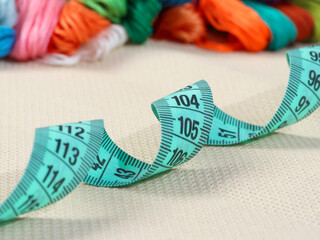 blue measuring tape lies in a wave on the fabric in the background multicolored floss threads