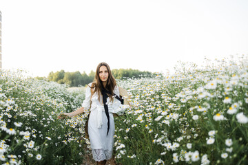 portrait of a beautiful young Caucasian woman on a chamomile field in a picturesque valley. a young lady in a white cotton dress and a straw hat. holds a bouquet of daisies. 