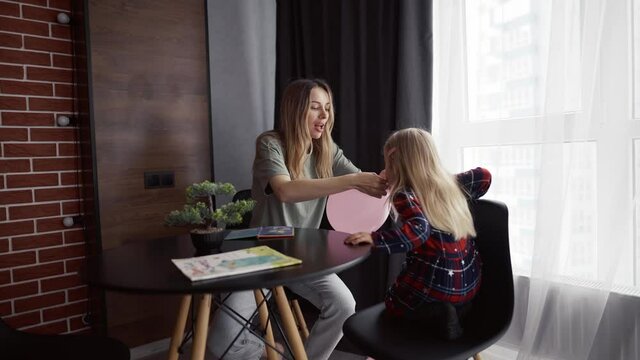 Little girl with loving mother babysitter inflates blowing air balloon