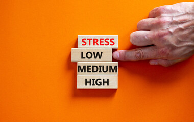 Low or high stress level symbol. Businessman chooses the wooden block with words low stress. Words stress low medium high. Beautiful orange background. Low or high stress level concept. Copy space.