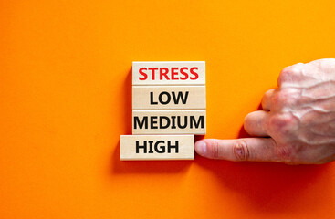 Low or high stress level symbol. Businessman chooses the wooden block with words high stress. Words stress low medium high. Beautiful orange background. Low or high stress level concept. Copy space.
