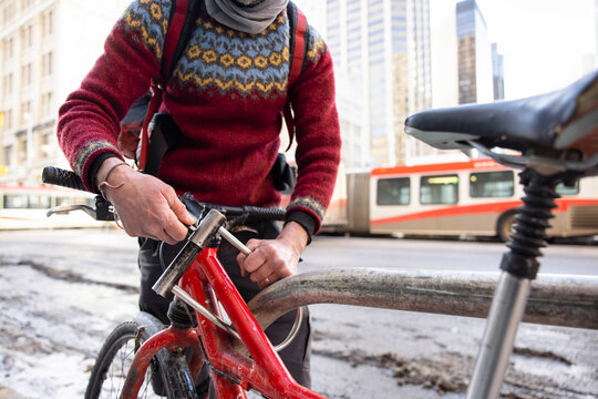 Male bike messenger locking bike to post on winter city sidewalk