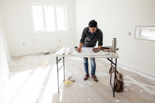 Male Architect Drafting Blueprints At House Construction Site