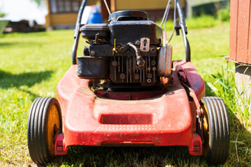 Close-up of an old red lawn mower. The surface is badly worn. Some of the parts are connected with a wire and a metal plate with self-tapping screws.