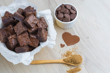 diced brownie pieces in a bowl on a wooden base, decorated with a brown sugar spoon, chocolate coins and a heart of cocoa powder