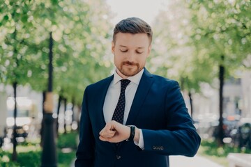 Attractive young man in elegant modern suit waiting for meeting in park