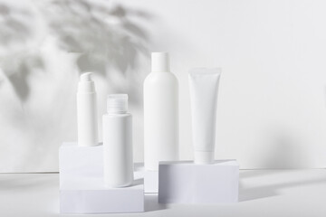 A set of white cosmetic jars on square stands with shadows. Toothpaste, face and body cream, hair...