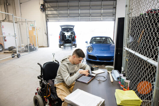 Disabled male body shop owner in wheelchair at desk in garage