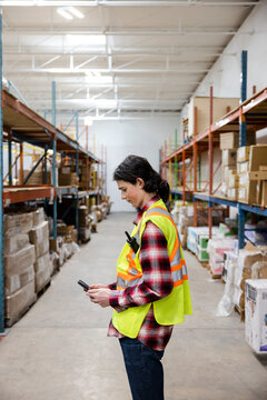 Male Warehouse Worker In Reflective Vest Using Smart Phone