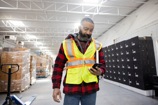 Male Warehouse Worker In Reflective Vest Using Smart Phone