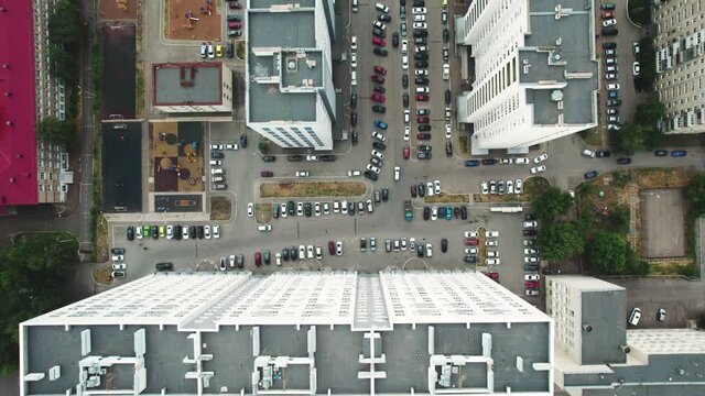 Aerial view of a residential apartment building in a city block. Drone flying over the roof of a house and a courtyard with many cars