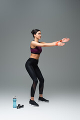 young sportswoman working out with elastics near sports bottle and dumbbells on grey background.