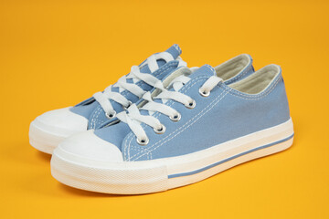 Pair of new blue sneakers, sport shoes on yellow background.