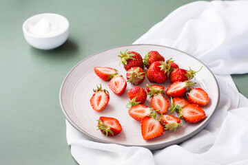 Fresh whole and sliced strawberries on a plate and sour cream in a bowl on a green background. Summer vitamin food