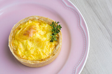 Lorraine cheese quiches with thyme detail on a pink plate, fuet on the side on a wooden base