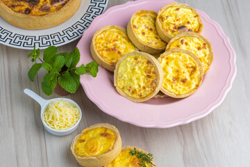 cheese lorraine quiches on a pink plate, some cheese and mint decorative elements, wooden base