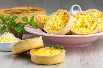 cheese lorraine quiches on a pink plate, some cheese and mint decorative elements, wooden base