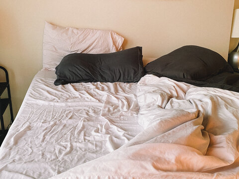 cozy hotel bed with white sheets, white pillows, and grey pillos
