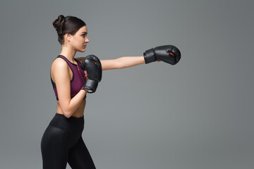 side view of woman in black sportswear boxing isolated on grey.